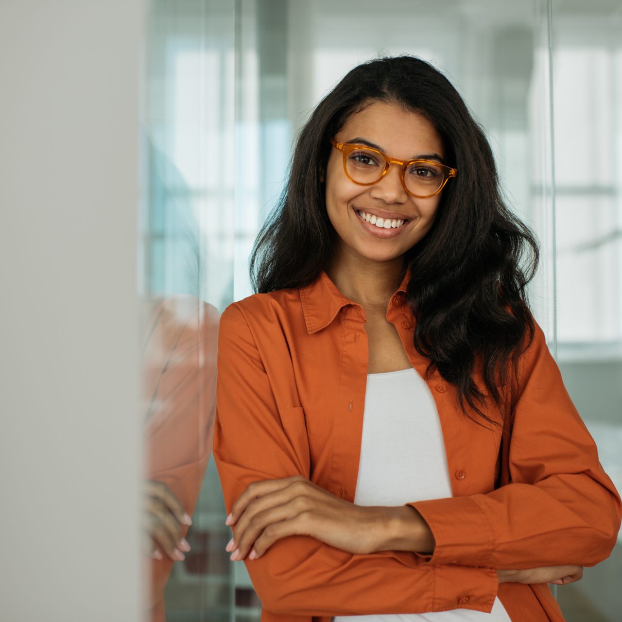 Portrait of smiling African American business woman wearing stylish eyeglasses looking at camera standing in modern office. Successful business and career concept